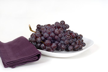 Image showing A bunch of juicy red grapes on a white plate with a purple napki