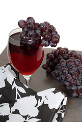 Image showing Glass of red wine with grapes and a black and white napkin