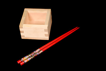 Image showing Wooden sake cup with chopsticks on black background