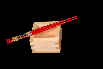 Image showing Wooden sake cup with chopsticks resting on top on black backgrou