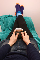 Image showing Woman holding a hot drink, relaxing with her feet up