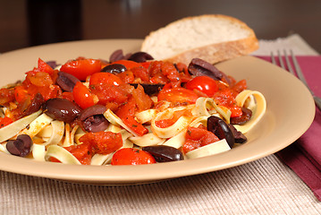 Image showing Closeup of a plate of pasta puttanesca with wine and bread