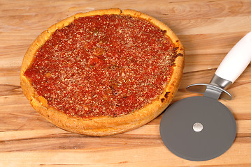 Image showing A Chicago style deep dish pizza on a cutting board with cutter