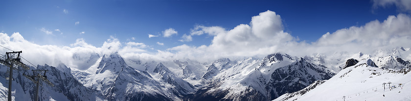 Image showing Panoramic view on ski slope and cloudy mountains at sun day