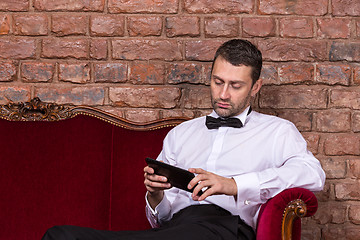 Image showing Businessman lying on a settee and reading tablet