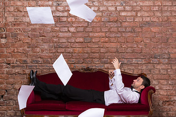 Image showing Businessman lying on a settee with flying papers