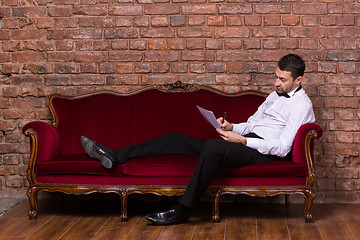 Image showing Businessman lying on a settee and reading paperwork