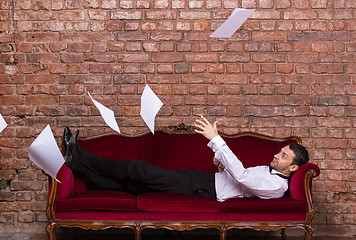 Image showing Businessman lying on a settee with flying papers