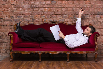 Image showing Businessman lying on a settee and reading paperwork