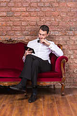 Image showing Businessman lying on a settee and reading tablet