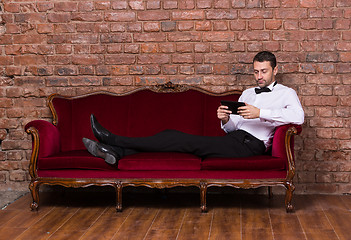 Image showing Businessman lying on a settee and reading tablet