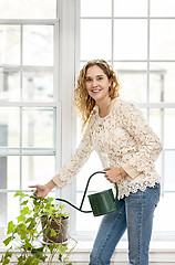 Image showing Smiling woman watering plant at home