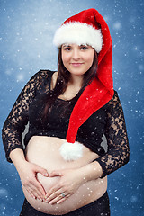 Image showing beautiful pregnant santa woman tenderly holding her tummy