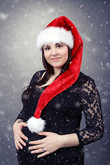 Image showing beautiful pregnant santa woman tenderly holding her tummy