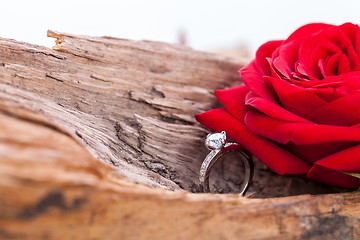 Image showing beautiful ring on wooden background and red rose