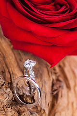 Image showing beautiful ring on wooden background and red rose