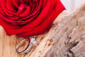 Image showing beautiful ring on wooden background and red rose