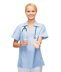 Image showing smiling doctor or nurse offering pills and water