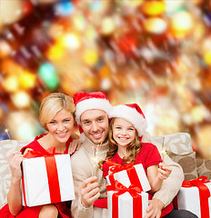 Image showing smiling family holding gift boxes and sparkles