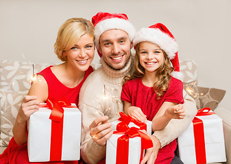 Image showing smiling family holding gift boxes and sparkles