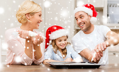 Image showing happy family in santa helper hats making cookies