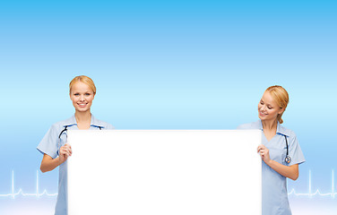 Image showing smiling female doctors or nurses with blank board