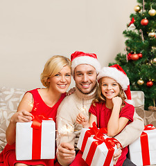 Image showing smiling family holding gift boxes and sparkles