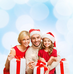 Image showing smiling family holding gift boxes and sparkles