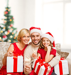 Image showing smiling family holding gift boxes and sparkles