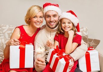 Image showing smiling family holding gift boxes and sparkles