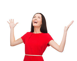 Image showing smiling young woman in red dress with hands up