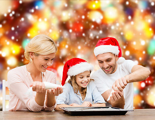 Image showing happy family in santa helper hats making cookies
