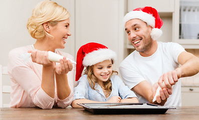 Image showing happy family in santa helper hats making cookies