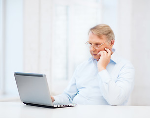 Image showing old man in eyeglasses working with laptop at home