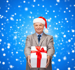 Image showing smiling man in suit and santa helper hat with gift