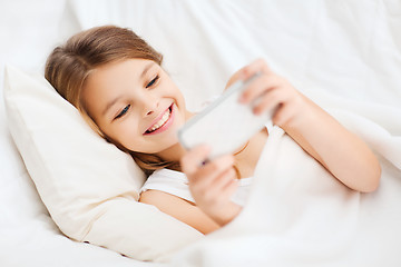 Image showing little girl with smartphone playing in bed