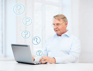 Image showing old man in eyeglasses working with laptop at home