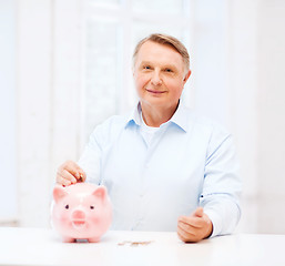 Image showing old man putting coin into big piggy bank