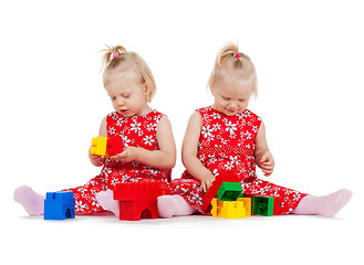 Image showing two twin girls in red dresses playing with blocks