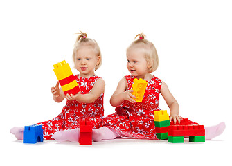 Image showing two twin girls in red dresses playing with blocks