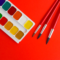Image showing paints and brushes on the red texture art palette