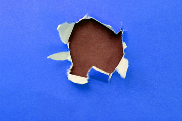 Image showing hole in the blue paper with ragged edges and brown texture