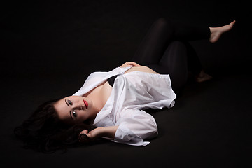 Image showing Portrait of long-haired woman in men's shirt lying on a black ba