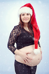 Image showing beautiful pregnant santa woman tenderly holding her tummy