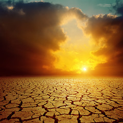 Image showing orange cloudy sunset over cracked desert