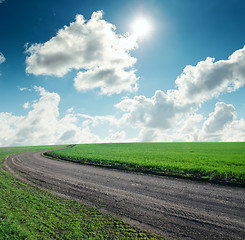 Image showing road in green grass under cloudy sky with sun