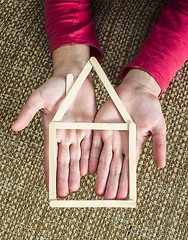 Image showing Hands holding model house made of wooden sticks