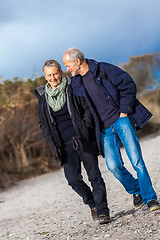 Image showing mature senior couple walking on the beach autumn winter