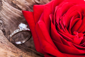 Image showing beautiful ring on wooden background and red rose