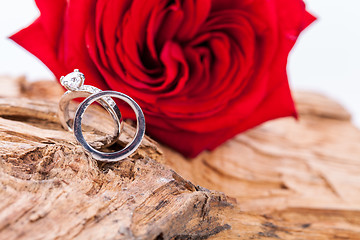 Image showing beautiful ring on wooden background and red rose